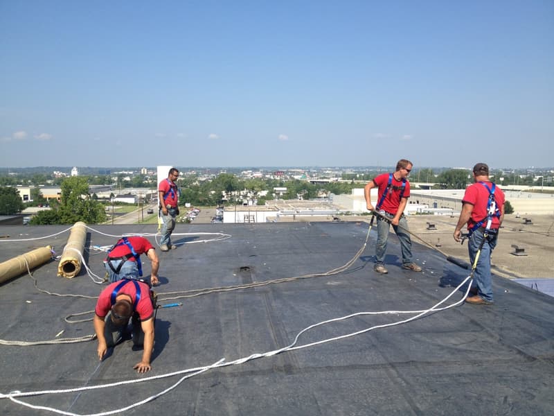 Crew in safety harnesses installing membrane on flat roof